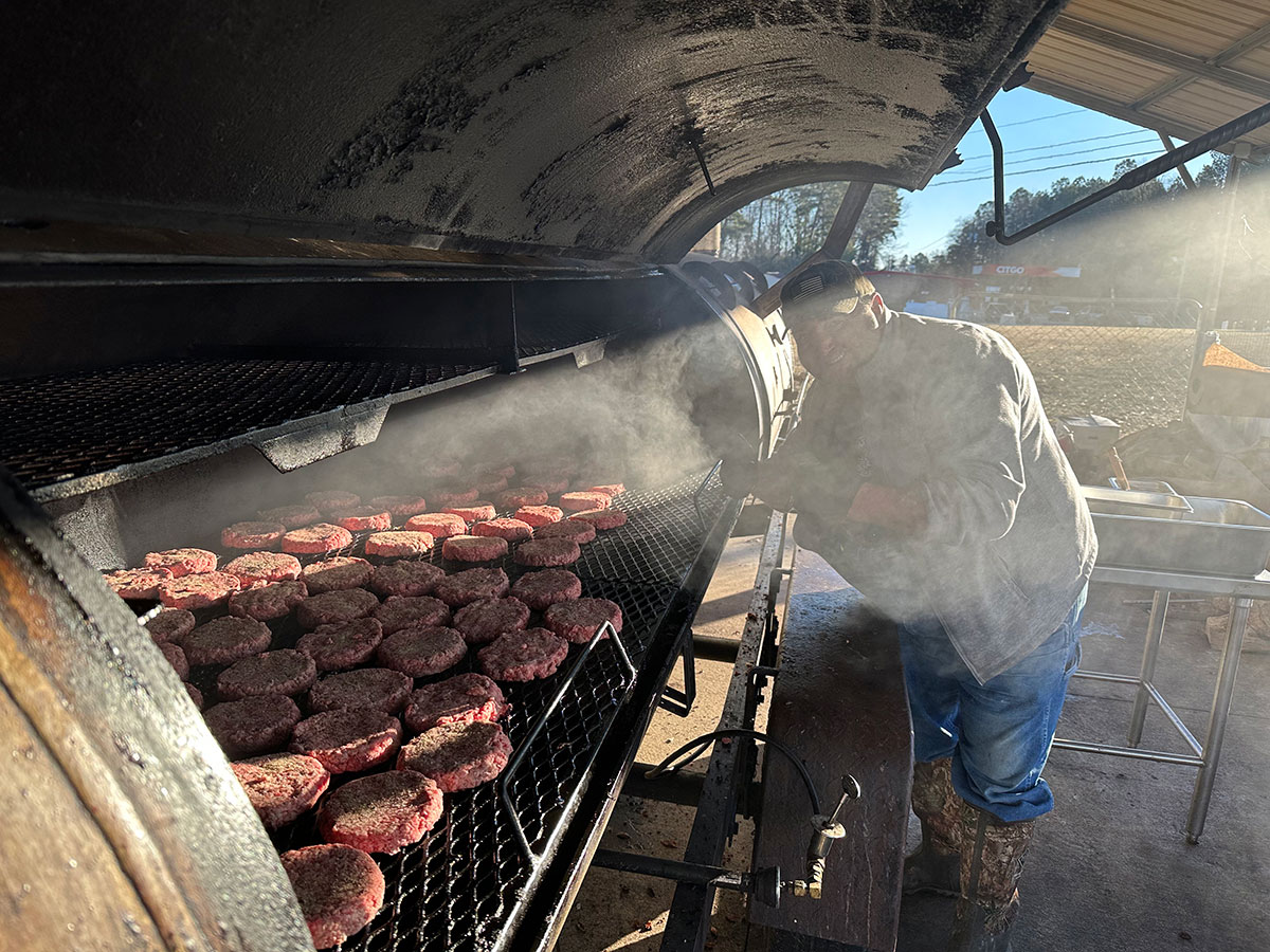 Burgers cooking over smoke on the Holy Smokes pit
