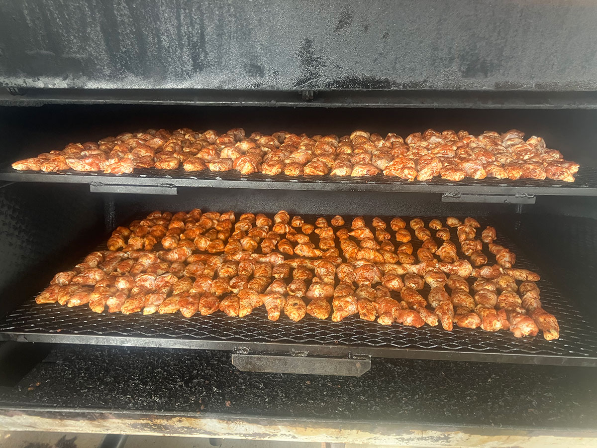 Pitmaster giving a thumbs up next to racks of smoked chicken