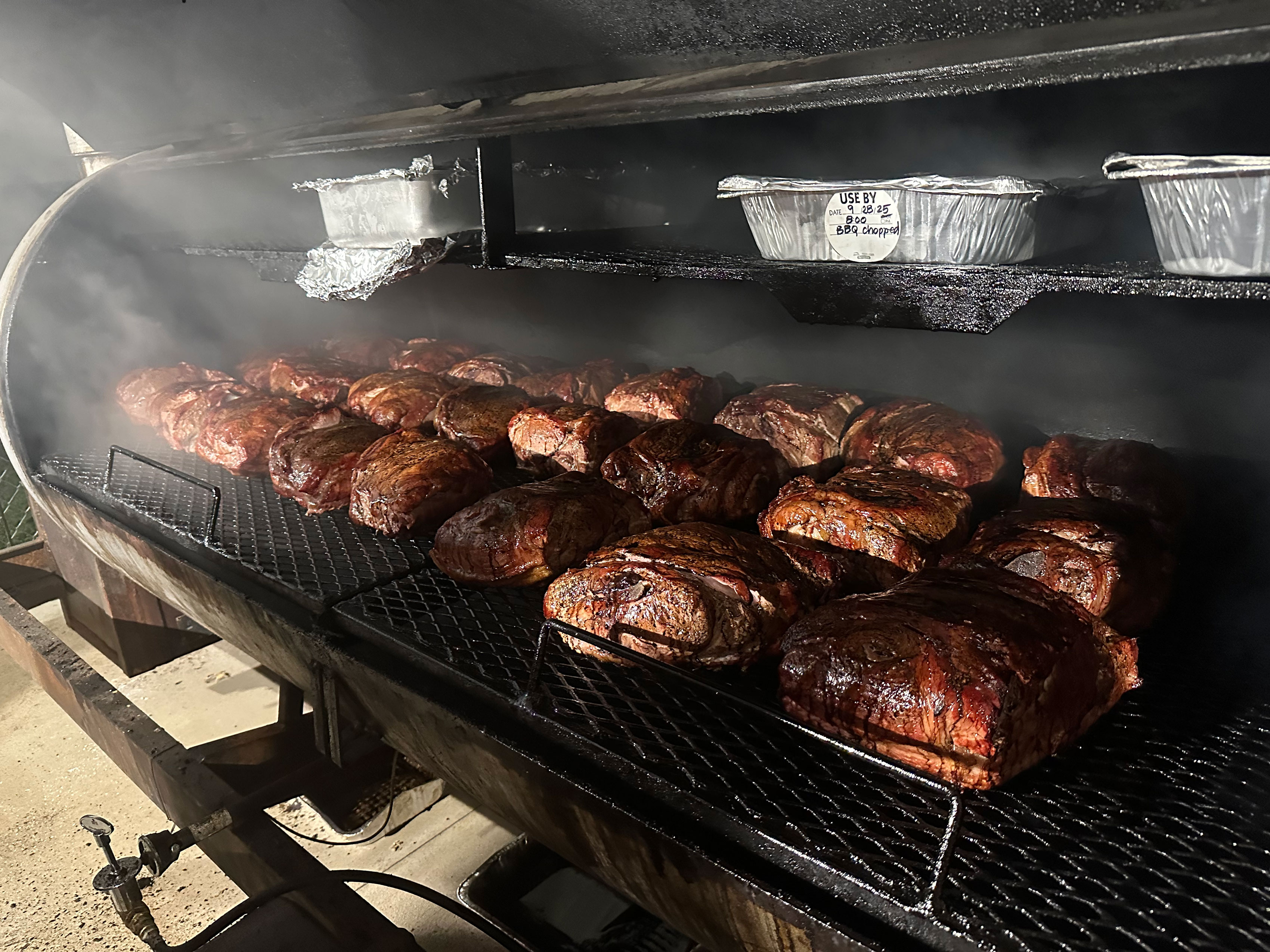 Racks of brisket and pork slow-smoking inside a Holy Smokes pit smoker